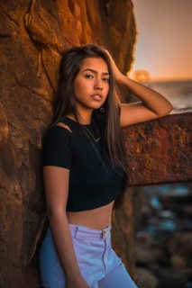A young pretty brunette Latina with long straight hair in a short black T-shirt and pink pants. Portrait of the woman leaning on a sculpture with scab