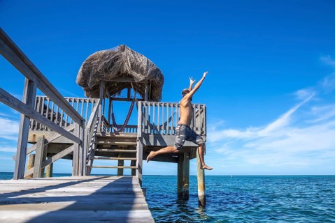 A young man throwing himself into the Caribbean Sea on Roatan Island from a wooden pier. Honduras