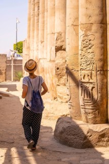 A young tourist in a white t-shirt and hat visiting the temple and looking at the ancient egyptian drawings on the columns of the Luxor Temple