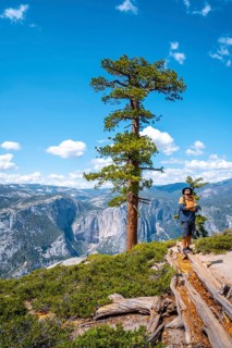 A young man with a brown jacket in Sentinel Dome looking at Upper Yosemite Fall