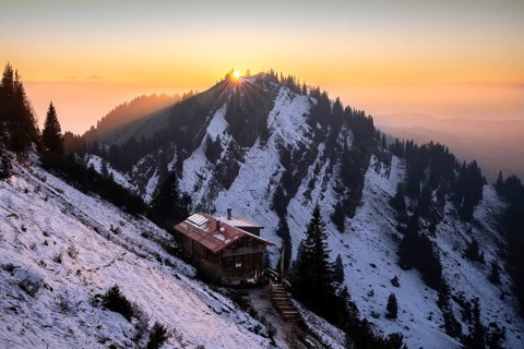 The Staufner Haus on the Hochgrat in autumn at sunset with backlight and sun star. There is snow on the slopes. Oberstaufen