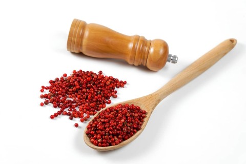 Pink peppercorns in a wooden spoon with a wooden pepper shaker isolated on a white background and copy space