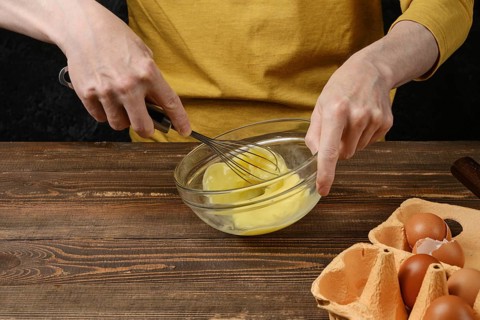 Unrecognizable man whisking eggs in a glass bowl while making an omelet