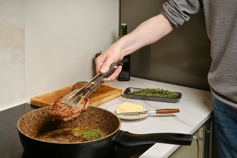 Close up view of taking out frying pan fried beefsteak with kitchen tongs