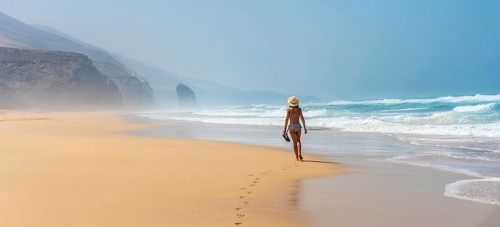 Panoramic of a young tourist with a hat walking alone on the Cofete beach of the Jandia natural park