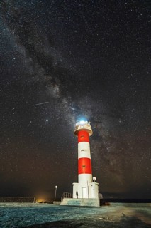 A young woman at the Fuencaliente Lighthouse with the milky way on the route of the volcanoes south of the island of La Palma
