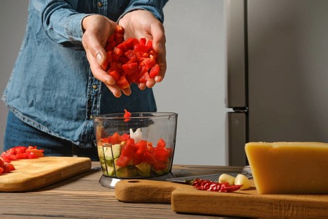 Close up view of female hands dropping chopped red bell pepper into blender in the kitchen