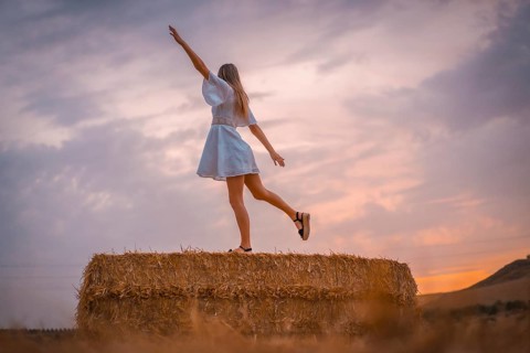 A young blonde Caucasian woman in a white dress in a field of dry straw atop a haystack. In a dry cultivated field in Navarra