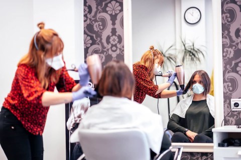 Hairdresser with mask and gloves smoothing hair of client dryer. Reopening with security measures for hairdressers in the Covid-19 pandemic