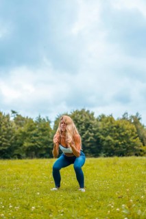 Fitness session with a young blonde caucasian woman exercising in nature with a blue maya on her feet and a white short shirt. Squatting and jumping