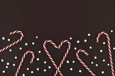 Christmas candy canes forming heart surrounded by white snowball ornaments on dark background