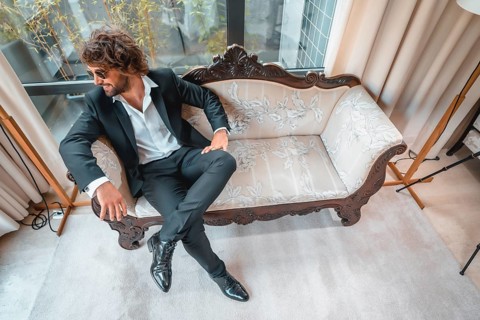 Street style with a young dark-haired caucasian man in a black suit and a white shirt in a luxurious hotel
