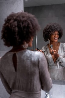 A young black girl with afro hair putting on makeup before the party with a smile. Exclusive party