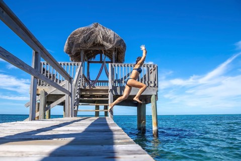 A young tourist girl throwing herself into the Caribbean Sea on Roatan Island from a wooden pier. Honduras