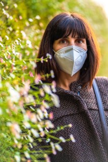 Portrait of a young woman with a mask next to a beautiful daisies. First walks of the uncontrolled Covid-19 pandemic