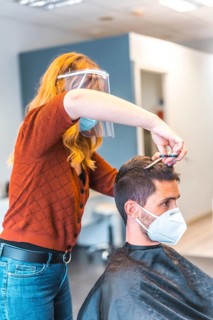 Hairdressers after the Coronavirus pandemic. Hairdresser with face mask and protective screen