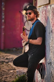 Hipster street musician in black playing electric guitar in the street on sunset leaning on a wall