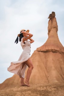 Brunette Caucasian model with a white dress and a straw hat in the Castildetierra of the Bardenas Reales desert