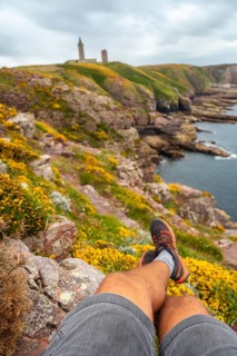 A young tourist sitting on the coast next to the Phare Du Cap Frehel