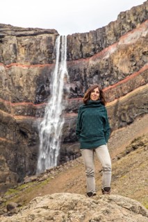 A young woman looking at the waterfall above Hengifoss from above. Iceland