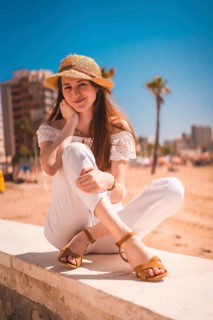 A Caucasian redhead dressed in white and with a straw hat on the beaches of Calpe