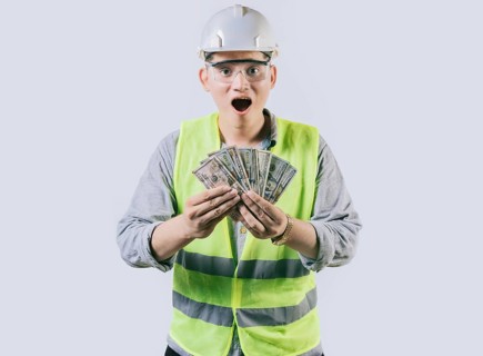Surprised engineer in helmet holding money isolated. Amazed male engineer holding banknotes on isolated background