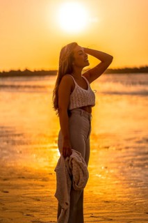 Summer lifestyle. A young blonde Caucasian woman in a white short wool sweater on a beach sunset. With eyes closed and enjoying the sea wind