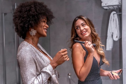 A young black girl with afro hair and a blonde Caucasian girl putting on makeup before the party with a smile. Exclusive party