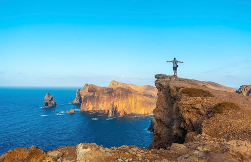 A young man on a cliff at Ponta de Sao Lourenco on the coast with rock formations in summer