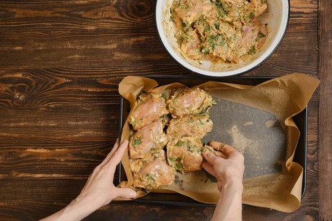 Hands of woman putting chicken thighs in baking tray from a bowl