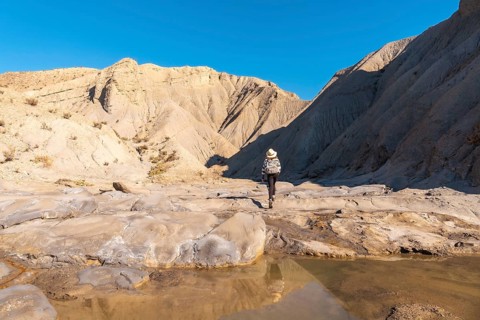A young woman walking along the water in the desert on a trek in the Travertino waterfall and Rambla de Otero in the desert of Tabernas