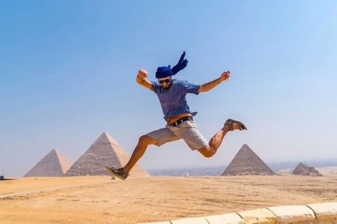 A young tourist jumping for joy in a blue turban and sunglasses at The Pyramids of Giza