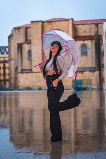 Posing of a young brunette Latina with a leather hat in the rain with a transparent umbrella in the city