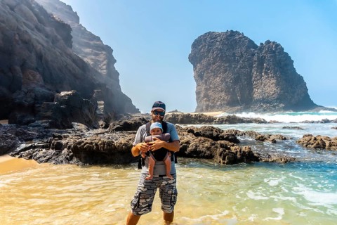 A young father with his baby in his backpack in the Roque del Moro of the Cofete beach of the natural park of Jandia