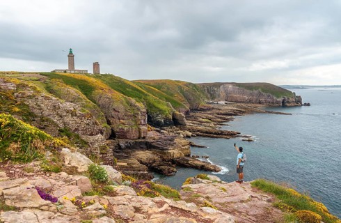 A young tourist taking a photo on the coast next to the Phare Du Cap Frehel