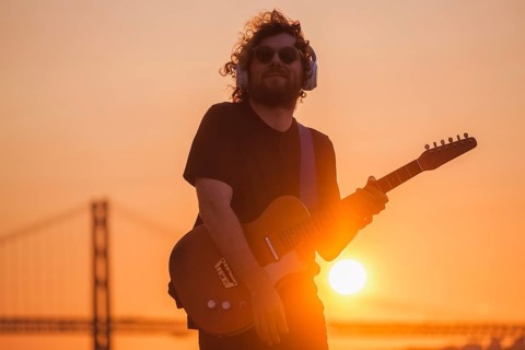 Hipster street musician in black playing electric guitar in street outdoors on sunset