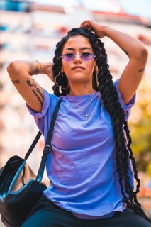 Portrait of young dark-skinned woman with long braids and purple glasses sitting on a bench in the park