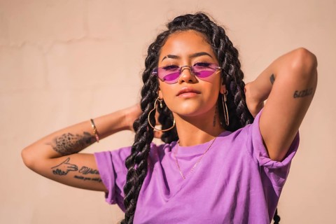 Urban session. Young dark-skinned woman with long braids wearing purple glasses on a plain background