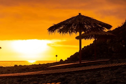 Orange sunset on the umbrellas at Ponta do Sol beach