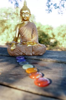 Statue of buddha in the field on a sunlit wooden table with chakra stones in a row