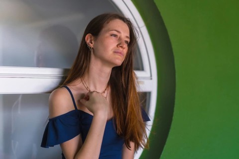 A young pretty redhead Caucasian girl smiling sitting in a blue dress next to a white sale of a green house