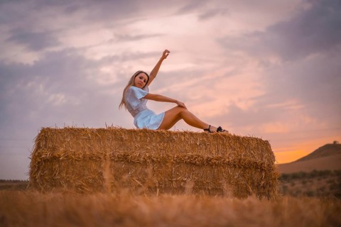 A young blonde Caucasian woman in a white dress in a field of dry straw atop a haystack. In a dry cultivated field in Navarra
