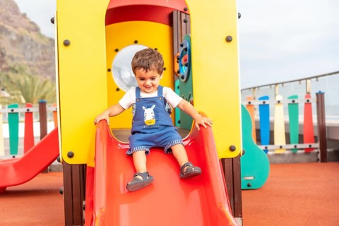 Boy playing in a playground having fun in summer and getting off the squeaker