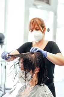 Hairdresser with mask and gloves combing the client. Reopening with security measures of Hairdressers in the Covid-19 pandemic