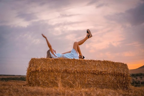 A young blonde Caucasian woman in a white dress in a field of dry straw atop a haystack. In a dry cultivated field in Navarra