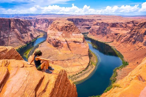 A tourist sitting on Horseshoe Bend and the Colorado River in the background