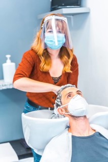 Hairdressers after the Coronavirus pandemic. Caucasian hairdresser with face mask and protective screen
