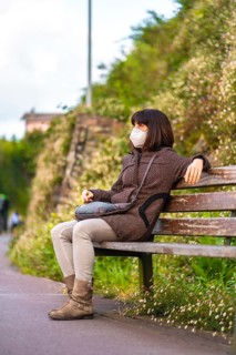Lifestyle of a young brunette with mask sitting on a wooden bench. First walks of the uncontrolled Covid-19 pandemic