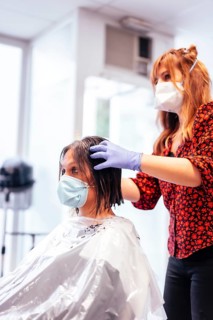 Hairdresser with mask and gloves showing the result to the client. Reopening with security measures for hairdressers in the Covid-19 pandemic