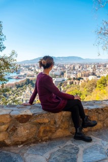 A young tourist sitting in spring looking at the views of the city and the Cathedral of the Incarnation of Malaga from the Castillo de Gibralfaro in the city of Malaga